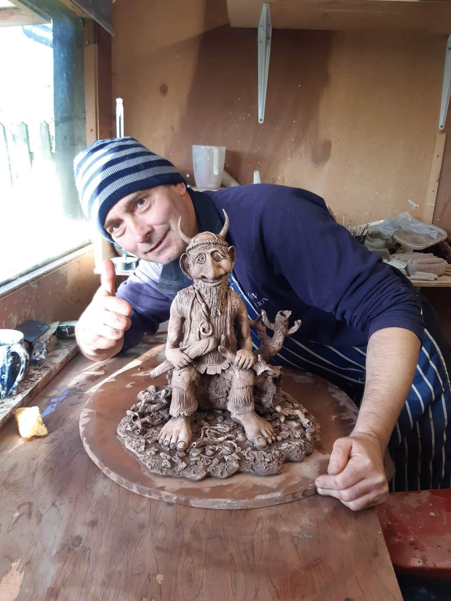 Nick at the workbench in his studio, holding up a finished sculpture.